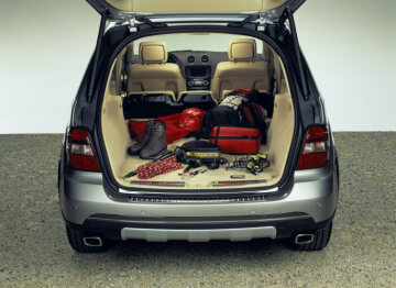 Mercedes-Benz M-Class, model series 164, 2005 version, studio shot, load compartment. Between 551 and 2050 litres (VDA measuring method) are available. The rear seats with backrests have a 63 : 37 folding split. The rear seat cushions can be swivelled into a vertical position behind the backrests of the front seats. The headroom under the open tailgate is 1.9 metres. The load can be easily secured to six lashing eyes and small items fit into the side stowage compartment. Available as special equipment: the EASY-PACK load-securing kit with load rails and removable rear seats as well as hydraulic operation of the tailgate.