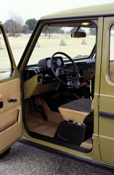 Mercedes-Benz 240 GD - 280 GE, Geländewagen, Baureihe 460, Version 1979, Serienlackierung Agavengrün (DB 6880). Interieur. Die Designer wählen zunächst eine einfache, zweckmäßige und funktionsgerechte Gestaltung mit lackierten Blechoberflächen und sparsamer Innenverkleidung. Durch das Zwei-Speichen-Lenkrad blickt der Fahrer auf eine einfache Instrumententafel mit Tachometer und Funktionsleuchten. Das Karomuster der Sitzflächen entspricht einer langjährigen Mercedes-Benz Tradition.