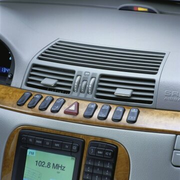 Mercedes-Benz S-Klasse, Baureihe 220, 1998 - 2002, Interieur Oriongrau, Holzausführung Kastanie (Sonderausstattung, Code 733). Mittig die logisch gruppierte Schalterleiste, darunter im "Drei-Insel-Design", eingelassen in Mittelkonsole und Dom, das Bedien- und Anzeigesystem COMAND sowie die serienmäßige Klimatisierungsautomatik mit Staub- und Aktivkohlefilter. Sie ermöglicht den Passagieren der S-Klasse die individiuelle Einstellung ihrer gewünschten Temperatur. Oben die Distanzanzeige des Parktronic-Systems (PTS, Sonderausstattung, Code 220) nach vorn.