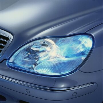 Mercedes-Benz S-Class, model series 220, 1998 version, exterior. Headlamps with driving light sensor (when activated, the exterior lighting switches on automatically at dusk, for example). On request for S 320, S 430 and S 500: xenon headlamps including dynamic headlamp range control. The headlamp cleaning system (standard on the S 430 and S 500) is included with the xenon headlamp option (code 612). Protective strip with chrome trim and the sensors for the PARKTRONIC system (PTS), below the headlamps.