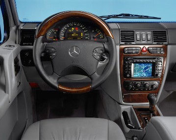 Mercedes-Benz G-Class, off-road vehicle, 463 series, 2000, interior. With the multifunction steering wheel, here in leather and wood design, information can be called up on the instrument cluster display, comfort settings can be made, and radio and navigation can be operated without taking your hands off the steering wheel. In the middle of the car, the console with the controls of the air conditioning and the switch groups for the all-wheel drive or the seat heating.