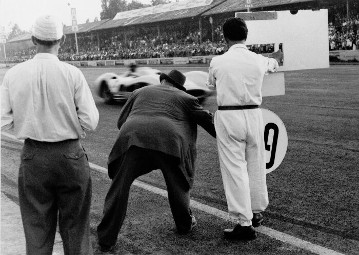 Großer Preis von Italien in Monza, 11.09.1955. Sieger Juan Manuel Fangio auf Mercedes-Benz Formel-1-Rennwagen W 196 R mit Stromlinienkarosserie, am Streckenrand Rennleiter Alfred Neubauer und Zeichengeber zeigt die Runde und den jeweiligen Abstand an.